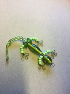 a green and black lizard with beads on it's body sitting on a table