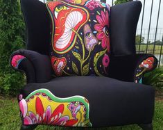 a black chair with colorful pillows on it sitting in the grass next to a fence