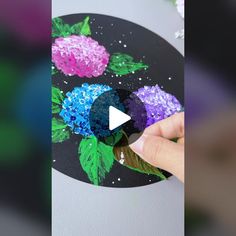 someone is painting flowers on a black plate with purple and blue glitters in the center