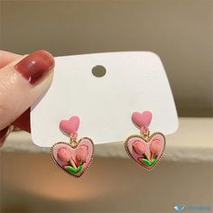 a pair of pink heart shaped earrings with flowers on them are being held up by a person's hand