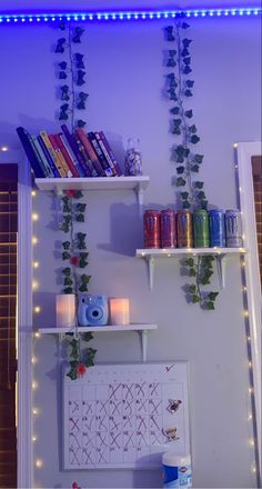 some shelves with books and candles on top of them in front of a purple wall