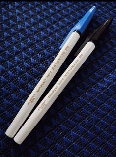 two white and blue pens sitting on top of a blue fabric covered surface with words written in black ink