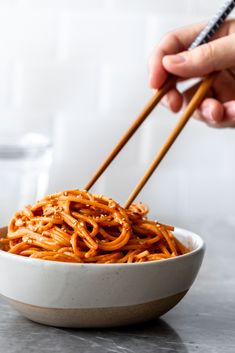 someone holding chopsticks over a bowl of noodles