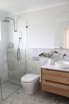 a white toilet sitting next to a walk in shower under a bathroom mirror above a sink