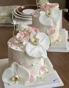 two wedding cakes decorated with white and pink flowers on top of each other, sitting on a wooden table