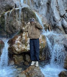 a man standing on top of a rock next to a waterfall