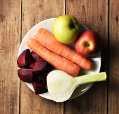 carrots, apples and onions are on a white plate with wood flooring in the background