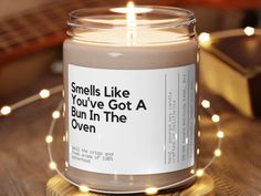 a candle is sitting on a table with some lights around it that says smells like you've got a bun in the oven