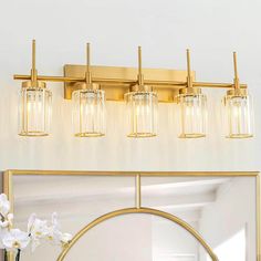 a bathroom vanity with a mirror and lights on the wall next to flowers in a vase