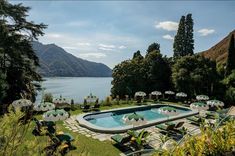 an outdoor swimming pool surrounded by lawn chairs and umbrellas with mountains in the background