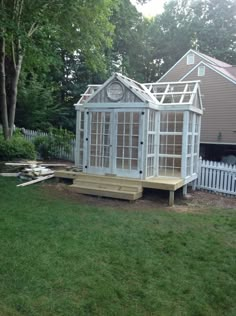 a small white house sitting on top of a lush green field next to a fence