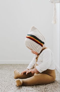 a baby sitting on the floor wearing a knitted hat