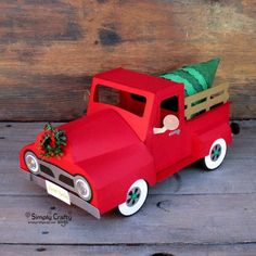 an old fashioned red truck with a christmas tree on the hood and windows is sitting in front of a wooden wall