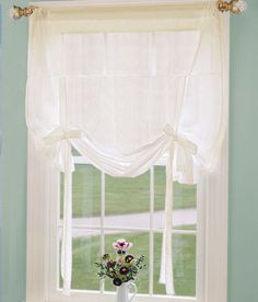 a vase with flowers sitting on a window sill in front of a white curtain