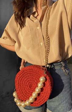 a woman holding a red purse with pearls on it