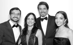 a group of people standing next to each other in front of a white wall wearing tuxedos