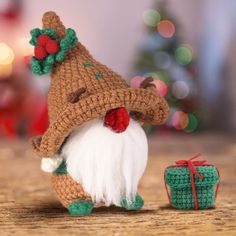 a crocheted christmas gnome next to a small gift box