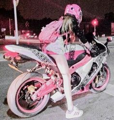 a woman sitting on top of a pink motorcycle in the middle of a street at night