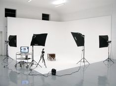 an empty studio with three lights and two stools in front of the white wall