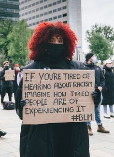 a woman with red hair holding a sign that says if you're tired of having about racism imagine how tired people are experiencing it