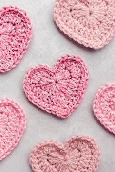 four crocheted hearts are arranged in pink and white on a light gray surface