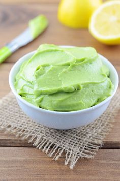 a white bowl filled with green frosting next to lemons on a wooden table