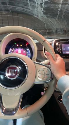 a person is driving a car with the steering wheel and dashboard lights on, while holding their hand up to the center console