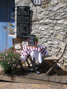 a table and chairs with a checkered table cloth on it in front of a stone building