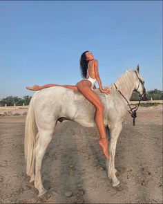 a woman sitting on top of a white horse in the dirt with her legs spread out