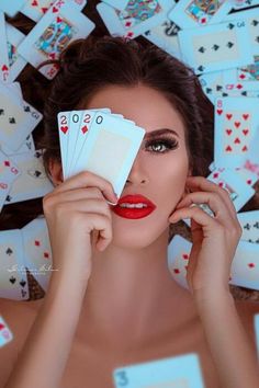 a woman holding up cards in front of her face and surrounded by other playing cards