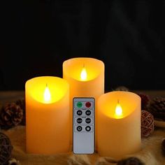 three lit candles sitting next to a remote control