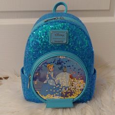 a blue backpack with princess on it sitting on top of a white fur covered floor