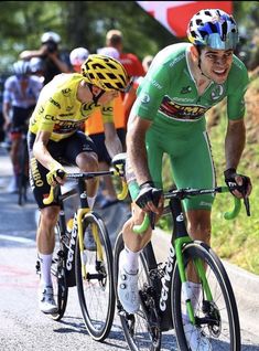 two bicyclists are racing down the road in front of other bicyclists