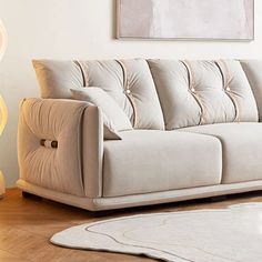 a white couch sitting on top of a hard wood floor next to a lamp and rug