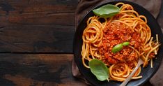 a plate of spaghetti with sauce and basil on a wooden table next to a fork