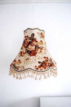 a lamp shade with flowers on it hanging from a ceiling fixture in a white room