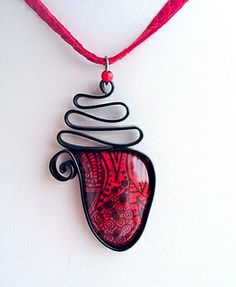 a red and black necklace with a wire wrapped around it on a pink cord hanging from a white wall