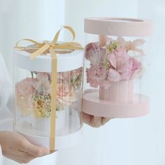 two boxes with flowers in them are being held by someone's hand and tied with a yellow ribbon