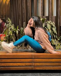 a woman sitting on top of a wooden bench talking on a cell phone and laughing