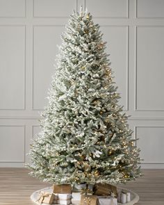 a white christmas tree with presents under it on a tray in front of a wall