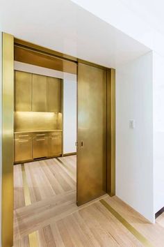 an empty room with wooden flooring and gold colored doors in the center is a kitchen