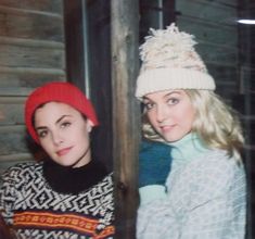 two women in winter clothes posing for a photo with one woman wearing a red hat