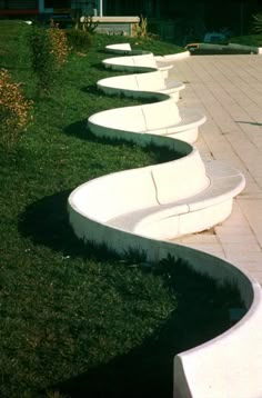 a row of white benches sitting on top of a grass covered field next to a building