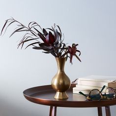 a gold vase with flowers and glasses on a table next to a stack of books