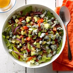 a white bowl filled with lettuce, tomatoes and other vegetables next to a glass of orange juice