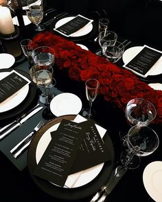 the table is set with black and white plates, silverware, and red roses