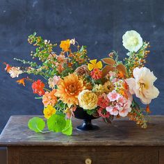 a vase filled with lots of different colored flowers on top of a wooden table next to a wall