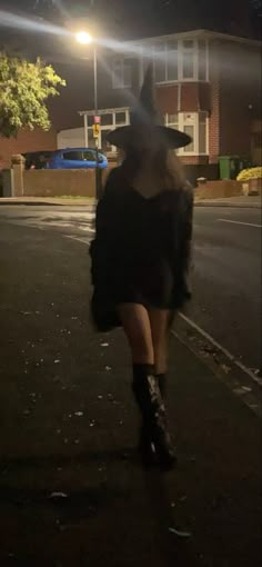 a woman walking down the street at night wearing boots and a black dress with long sleeves