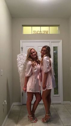 two beautiful young women standing next to each other in front of a door with angel wings