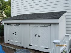 a white garage with three doors and a black roof on the side of a house